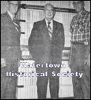 A group of men standing in front of a bookcase

Description automatically generated